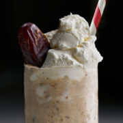 Light brown milkshake with a whipped cream topping, date garnish, and red and white striped straw.