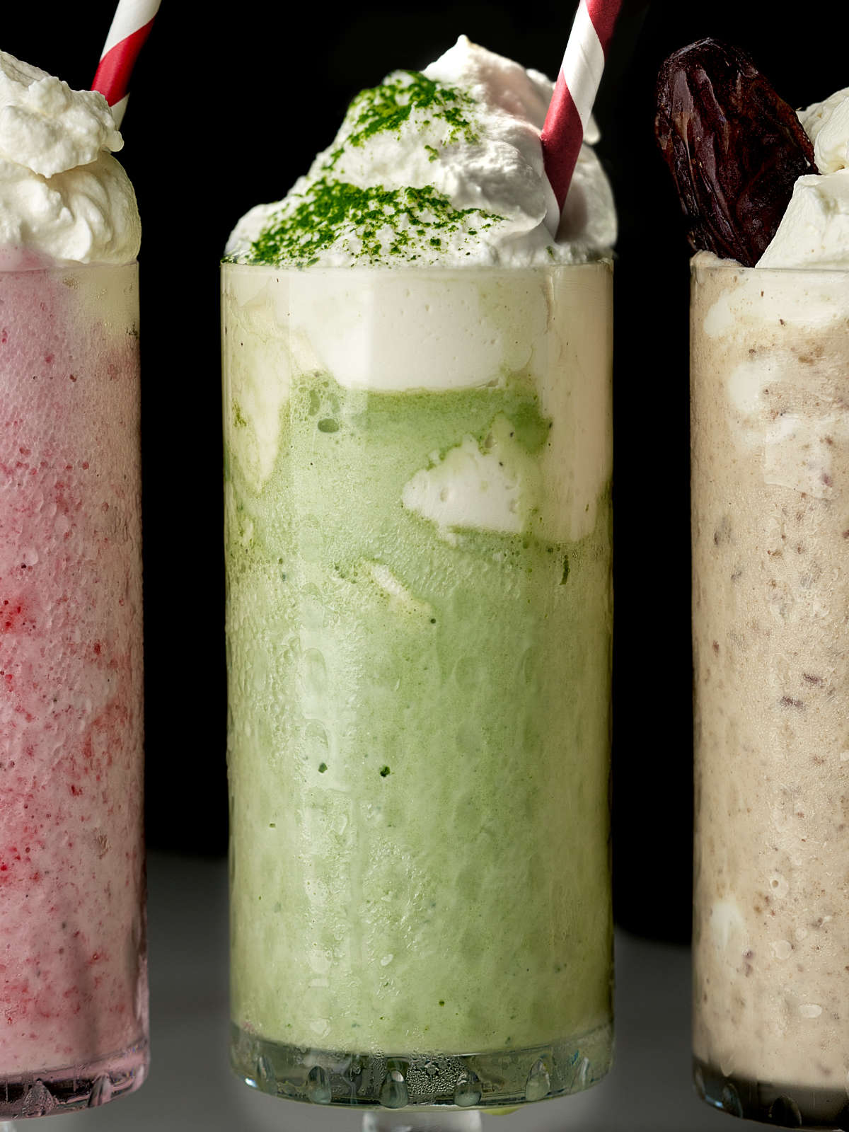 Green milkshake in between and pink milkshake and a light brown milkshake, all with red and white striped straws.