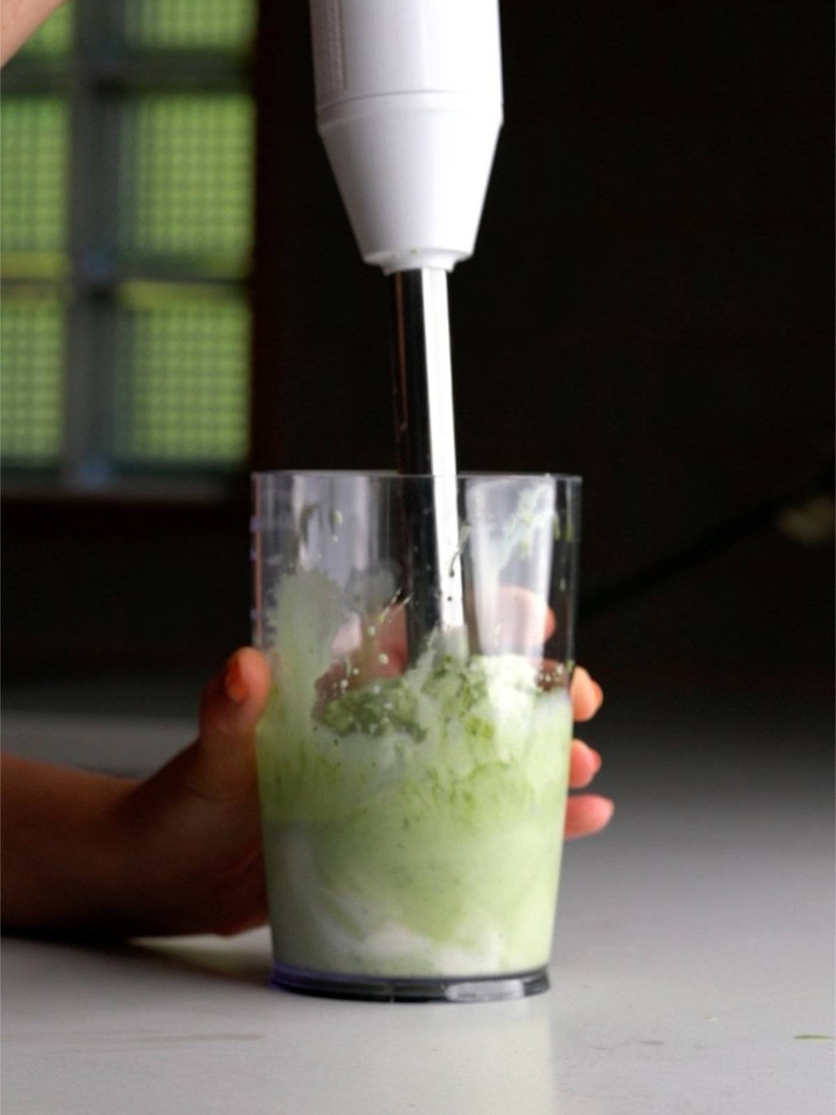 Blending vanilla ice cream with green matcha in a clear plastic container.