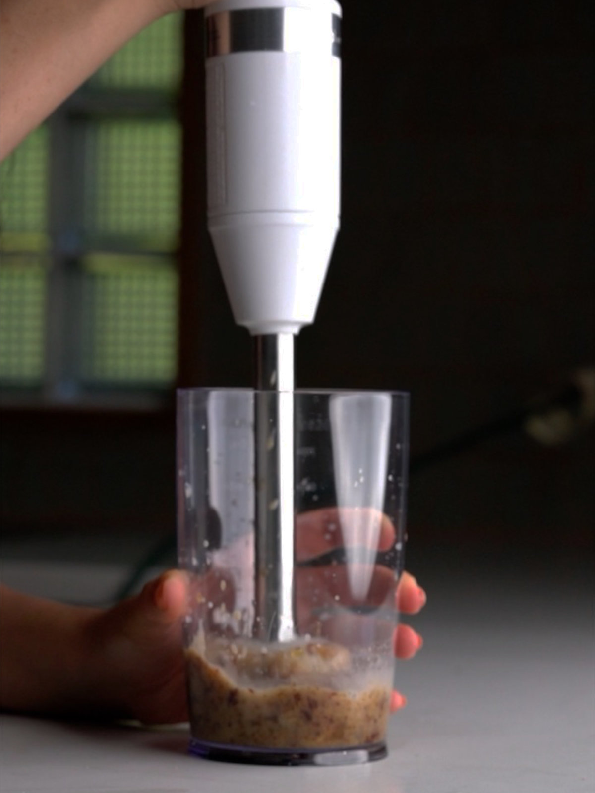 Immersion blender blending dates and a little milk in a clear container.