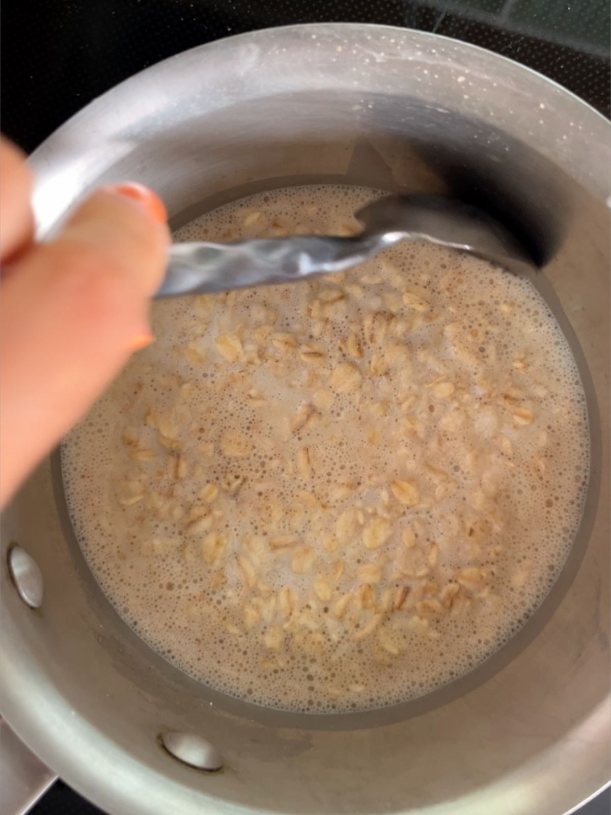 Metal spoon stirring oatmeal in a metal pot.