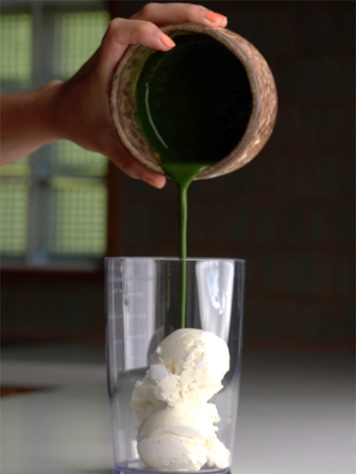 Pouring thick matcha into a container with vanilla ice cream.