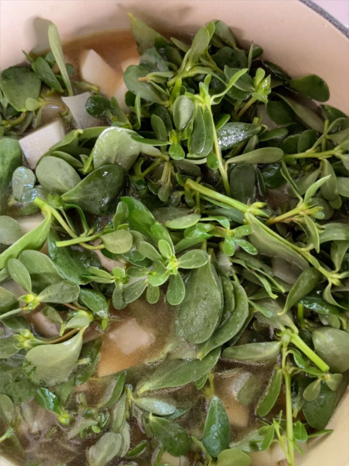 Purslane and diced potatoes in a soup pot.