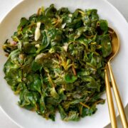 Sauteed greens in a white dish with gold serving utensils.