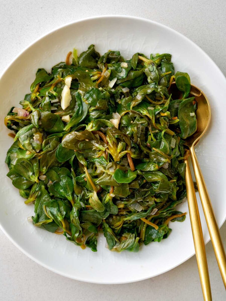 Sauteed greens in a white dish with gold serving utensils.