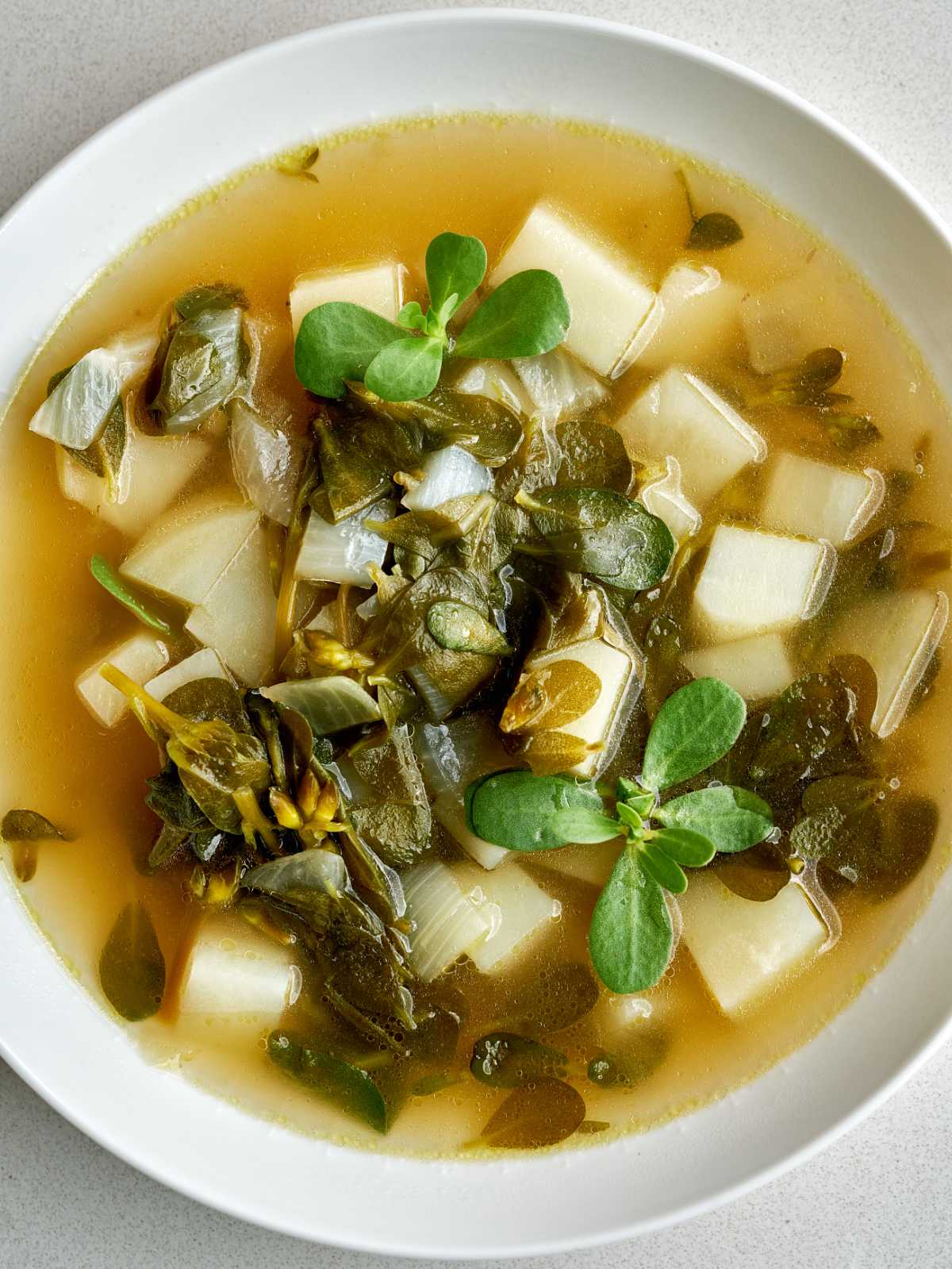 Purslane and potato cubes in a soup with a broth base.