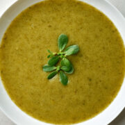 Green pureed soup with a sprig of purslane in the center.