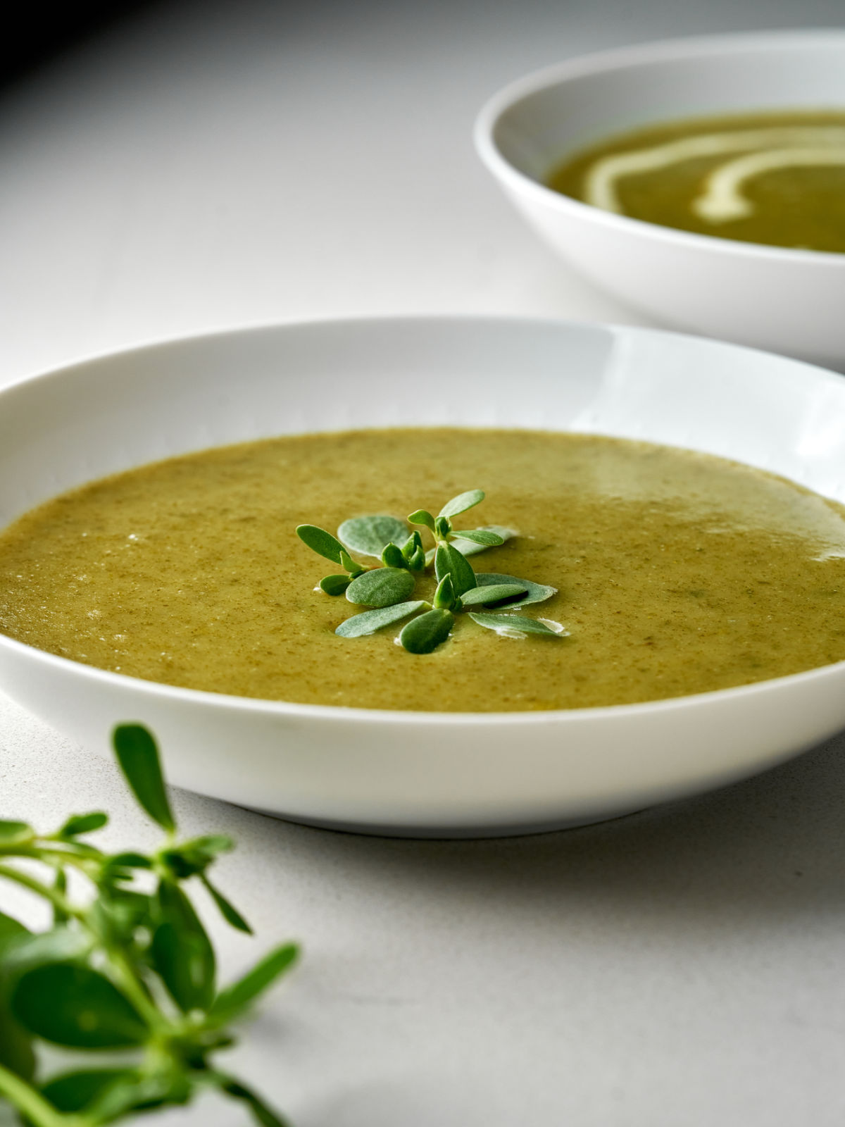 Two bowls of soup with green puree and sprigs of purslane.