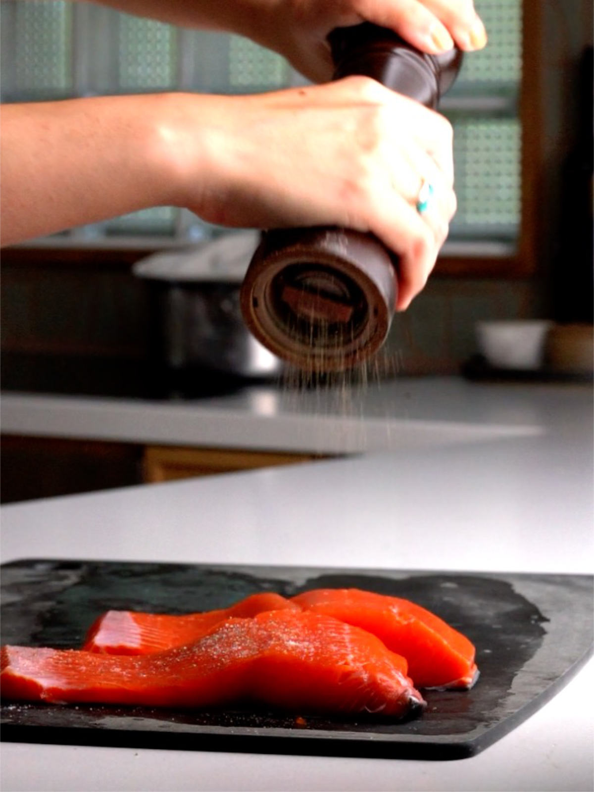 Cracking pepper over two salmon filets on a black cutting board.
