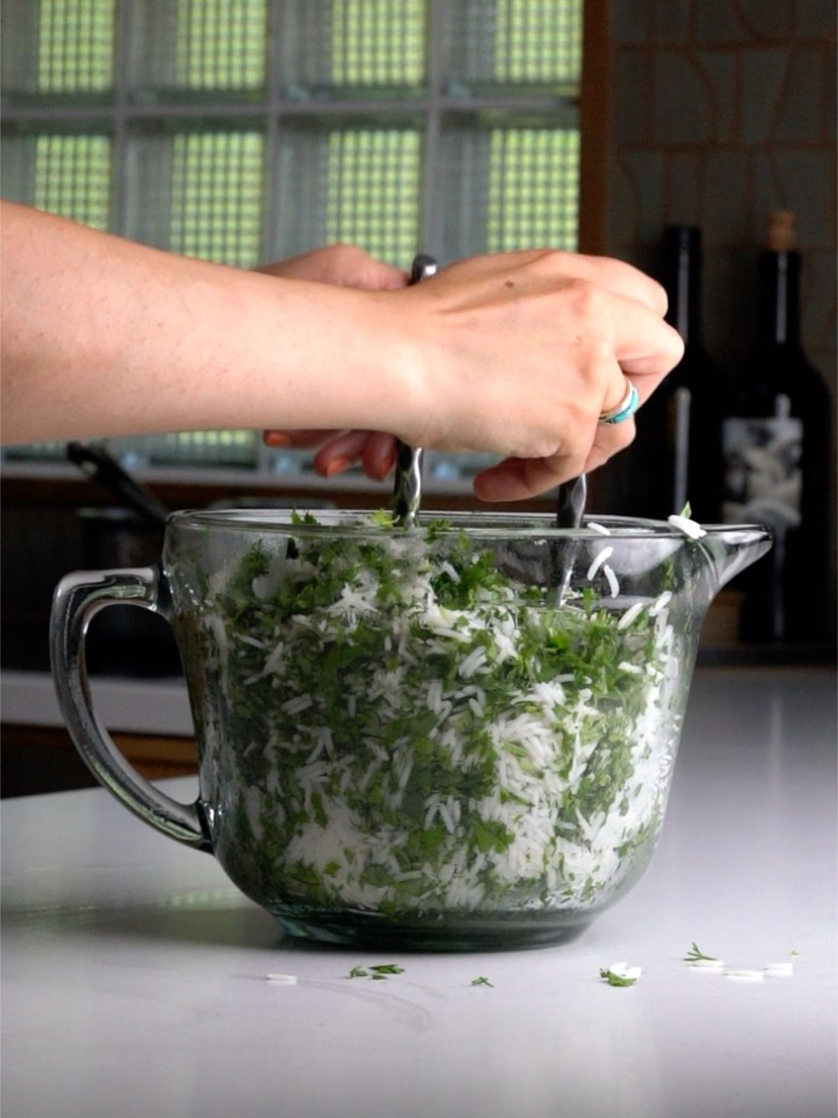 Mixing herbs and rice together in a large glass bowl with a spout and a handle.
