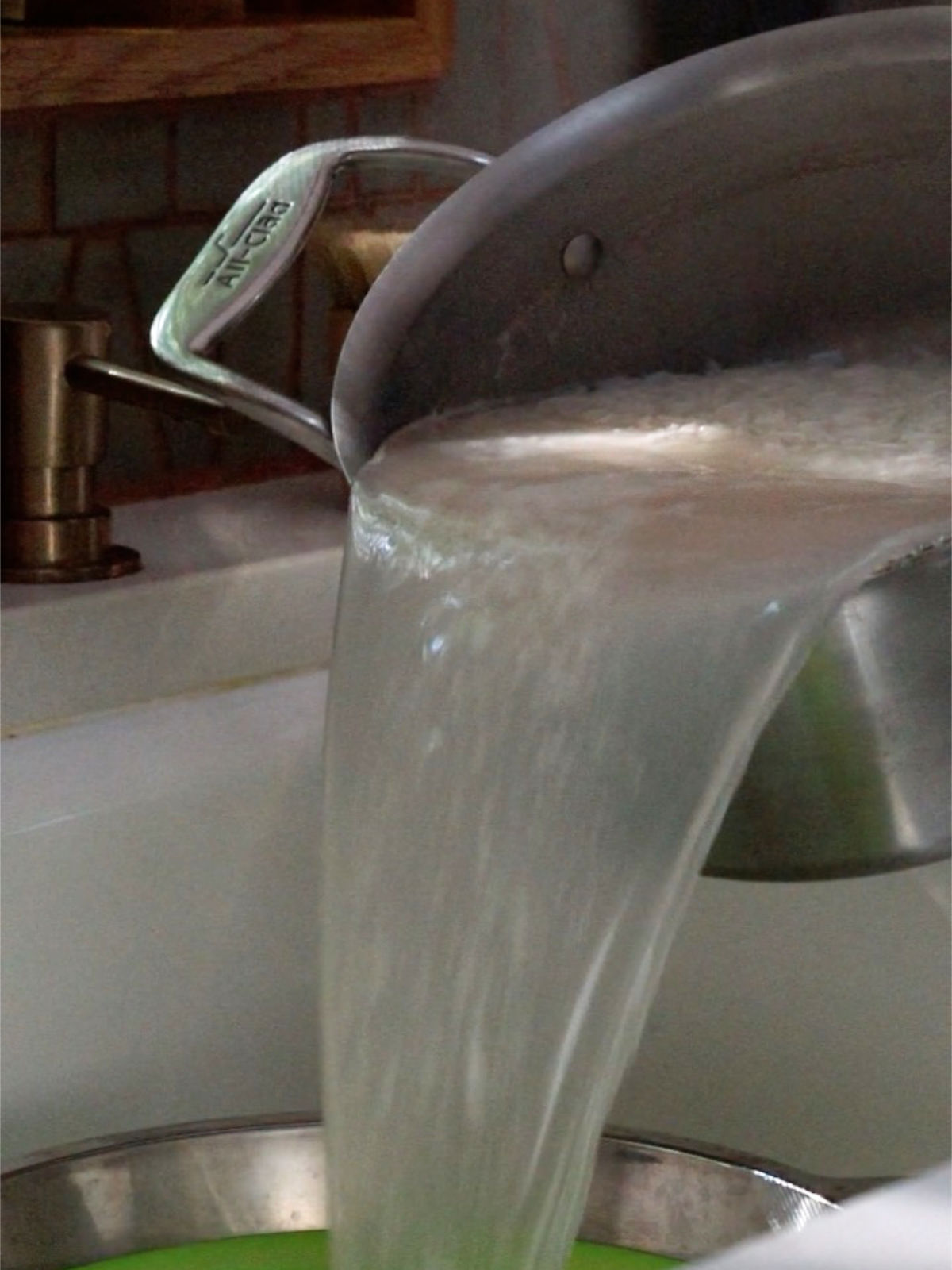 Pouring water out of a metal pot into a colander in a sink.