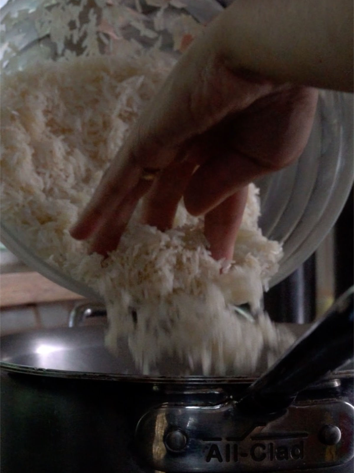 Pouring rice from a glass bowl into a metal pot.