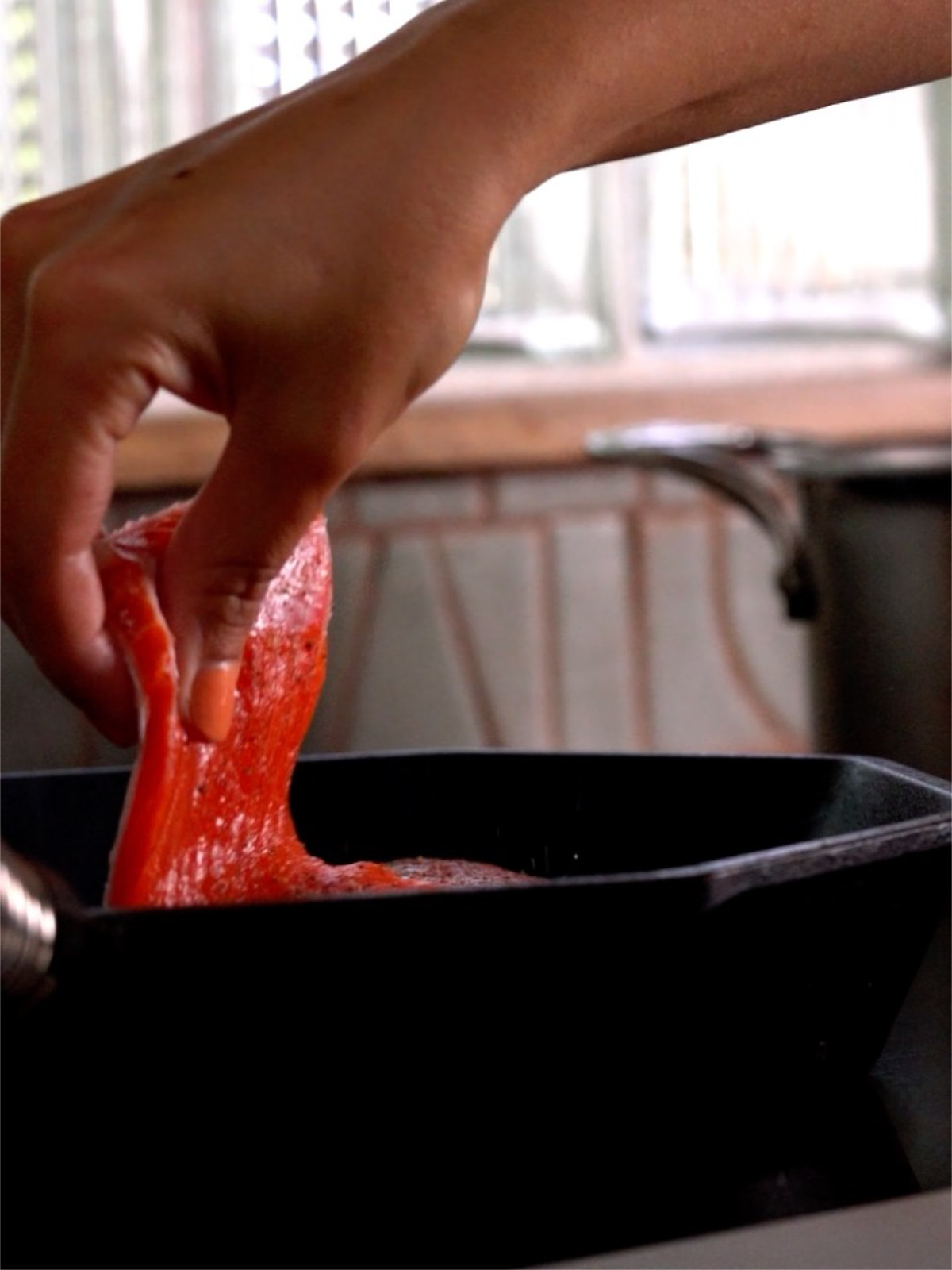 Hand placing a salmon filet in a cast iron pan.