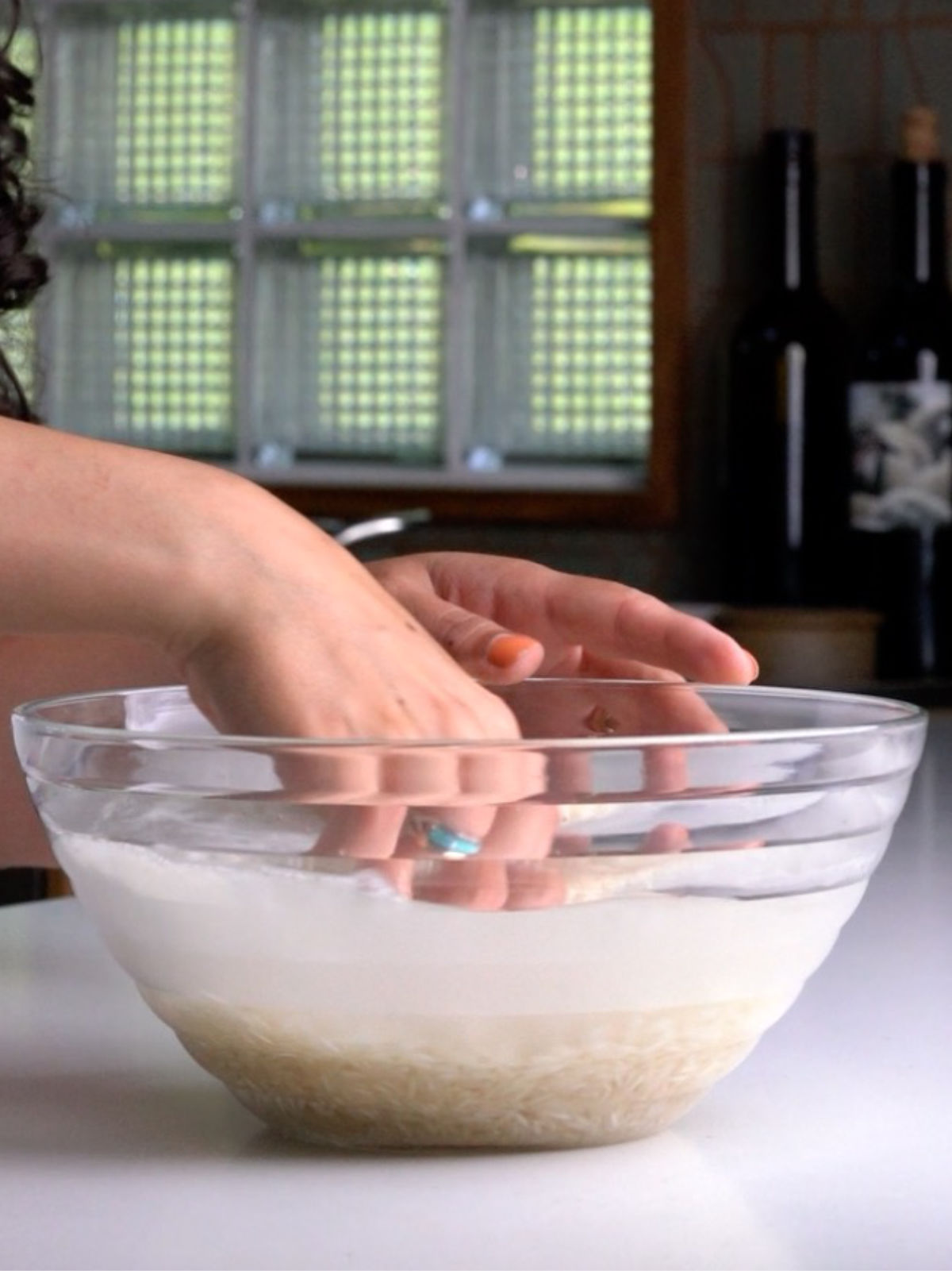 Hand washing rice in a glass bowl.
