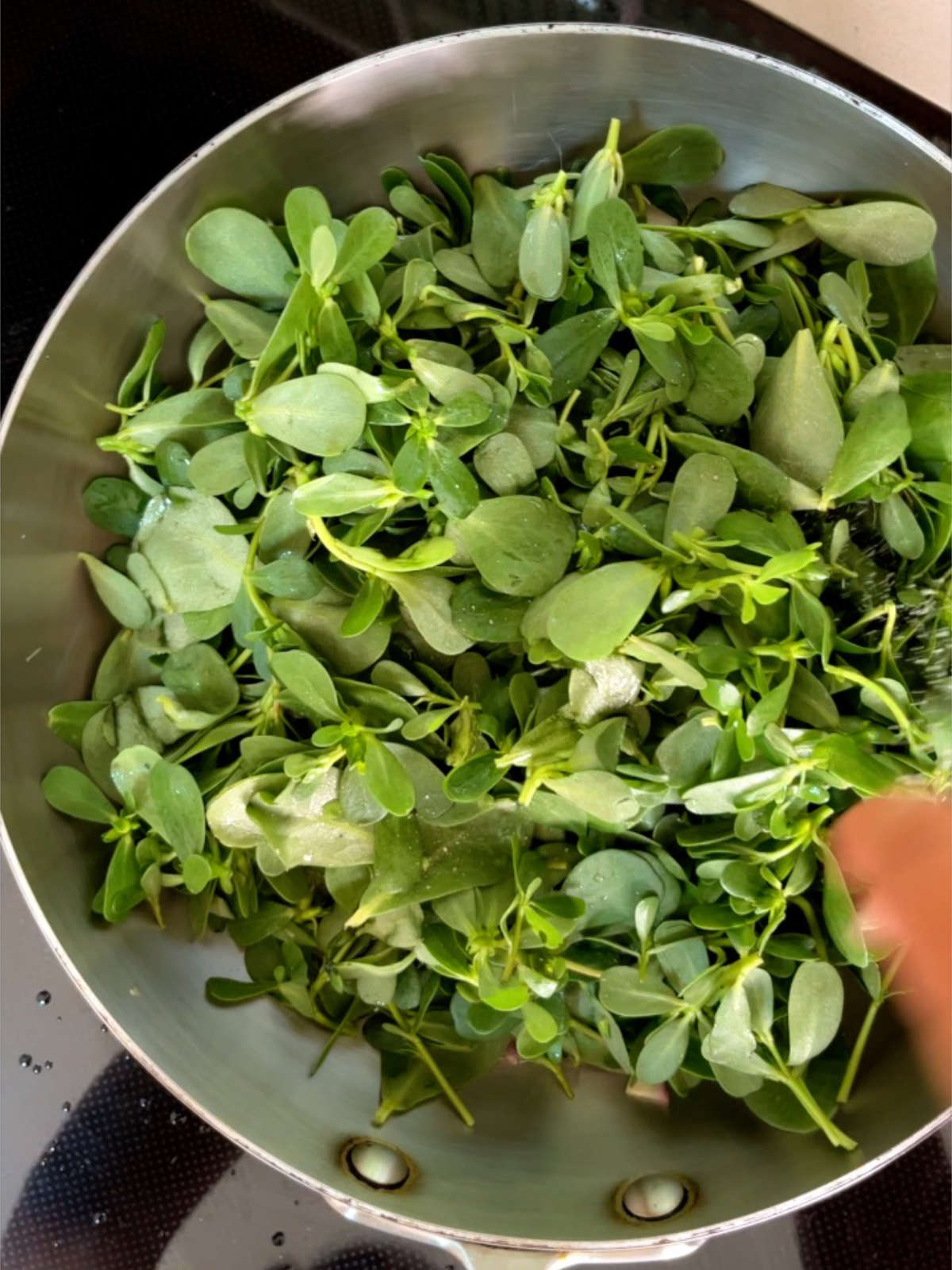 Greens filling a metal pan on a black cooktop.