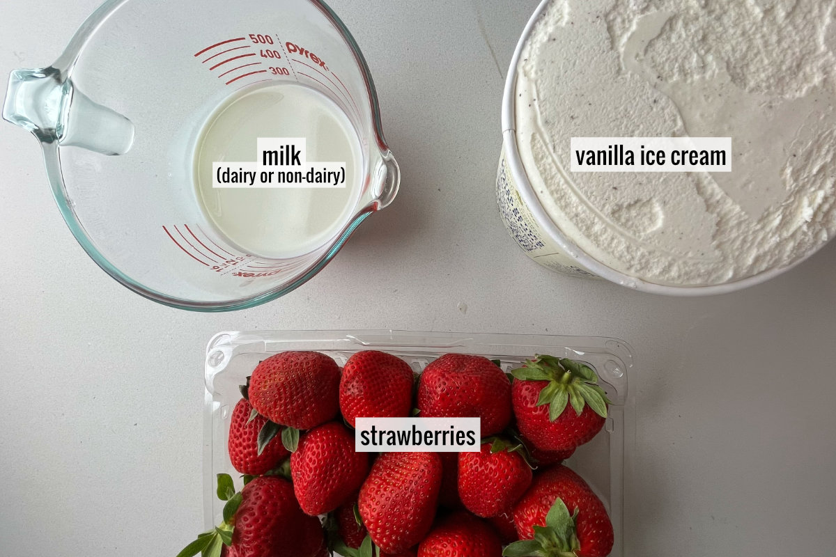 A carton of vanilla ice cream next to milk in a measuring cup on top of a plastic container with fresh strawberries.