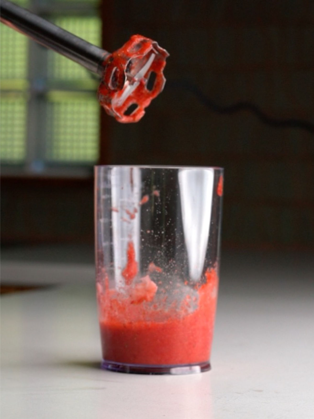 Strawberry puree in a clear container with an immersion blender above it.