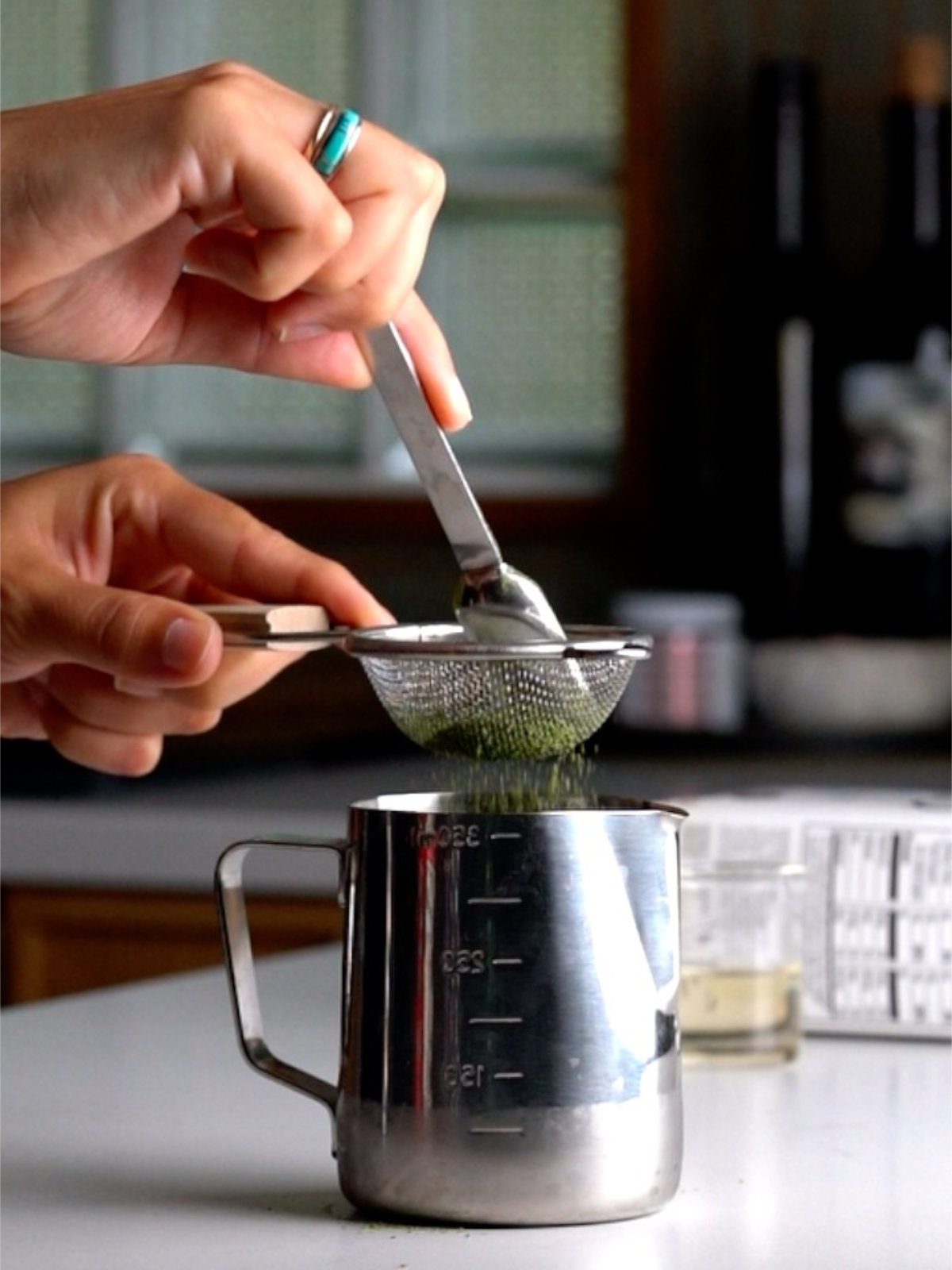Sifting matcha powder into a metal measuring cup.
