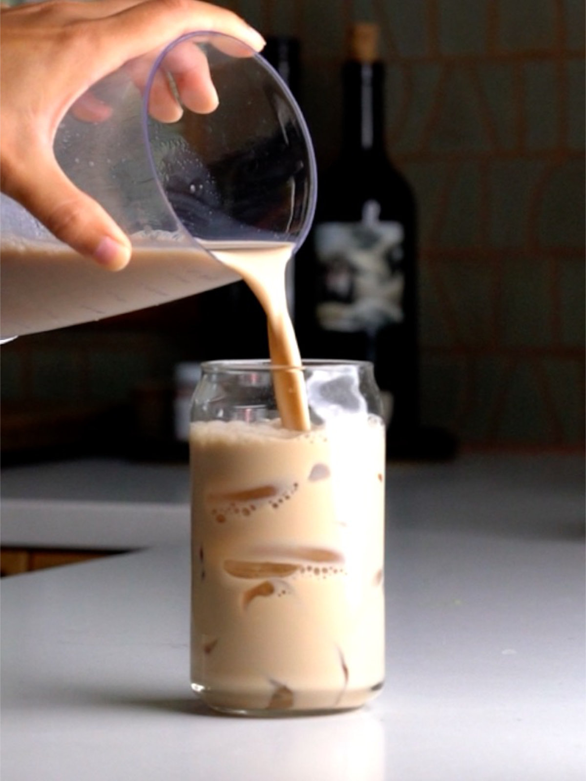 Pouring a chai latte into a glass filled with ice.