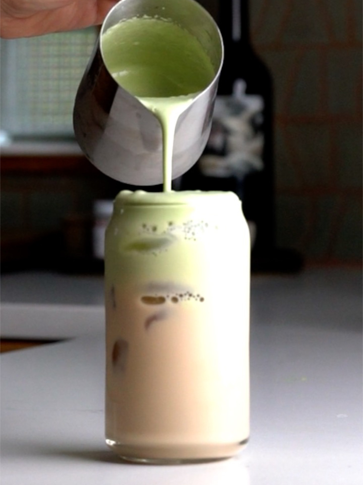 Pouring matcha foam over an iced chai latte.