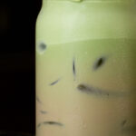 Ombre iced latte fading from green at the top to a light brown at the bottom with a black background.