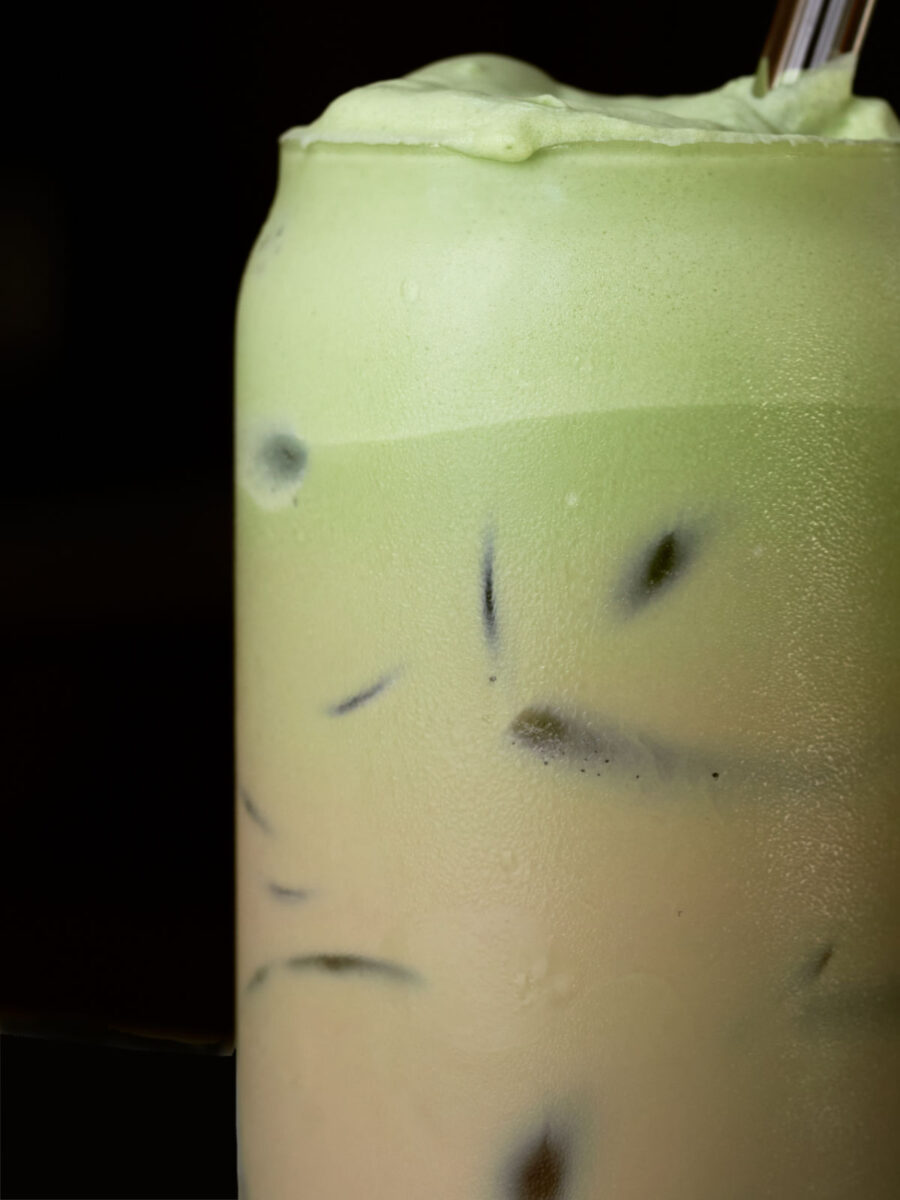Ombre iced latte fading from green at the top to a light brown at the bottom with a black background.