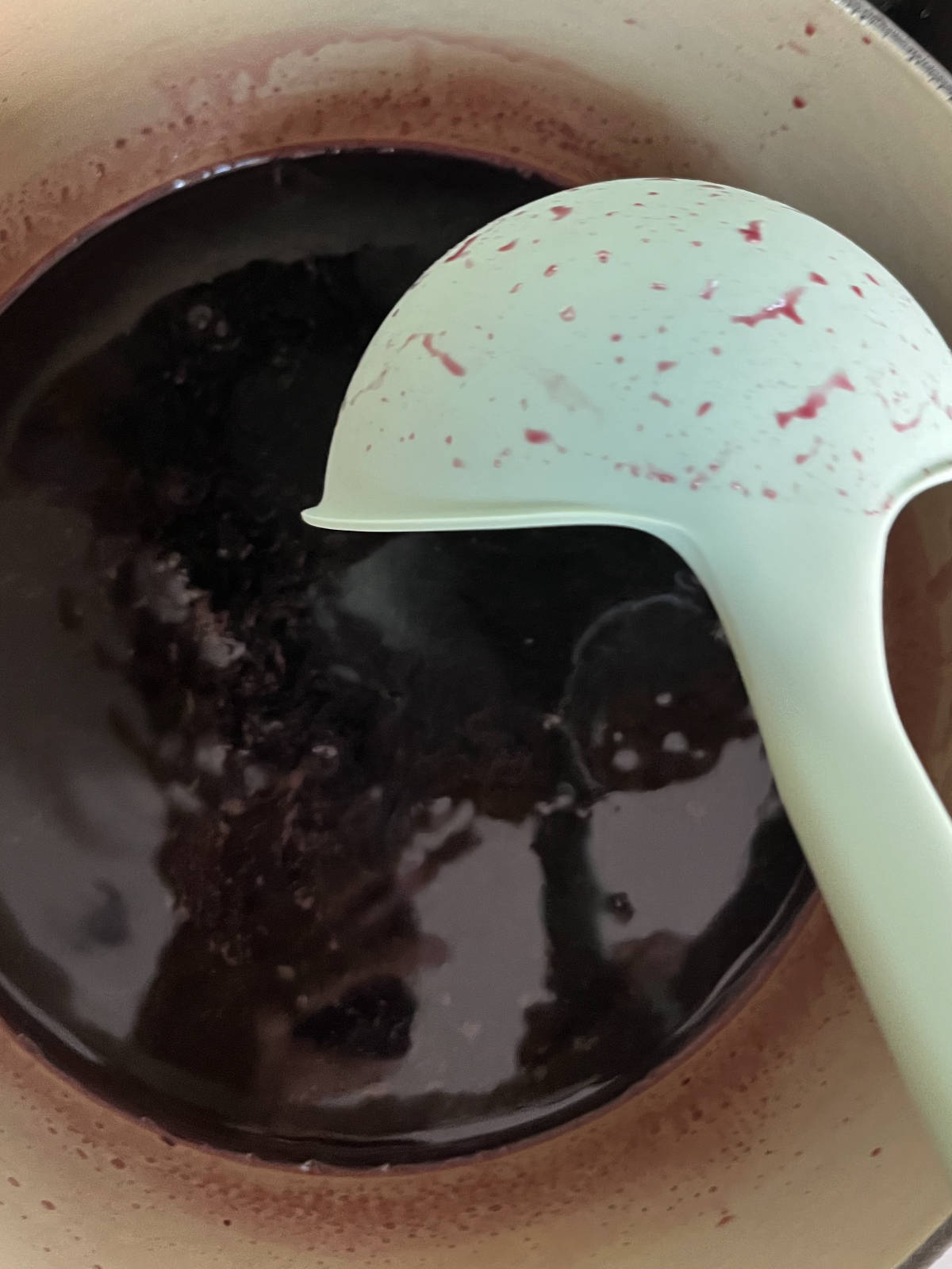 MInt colored ladle stirring burgundy liquid in a ceramic pot.