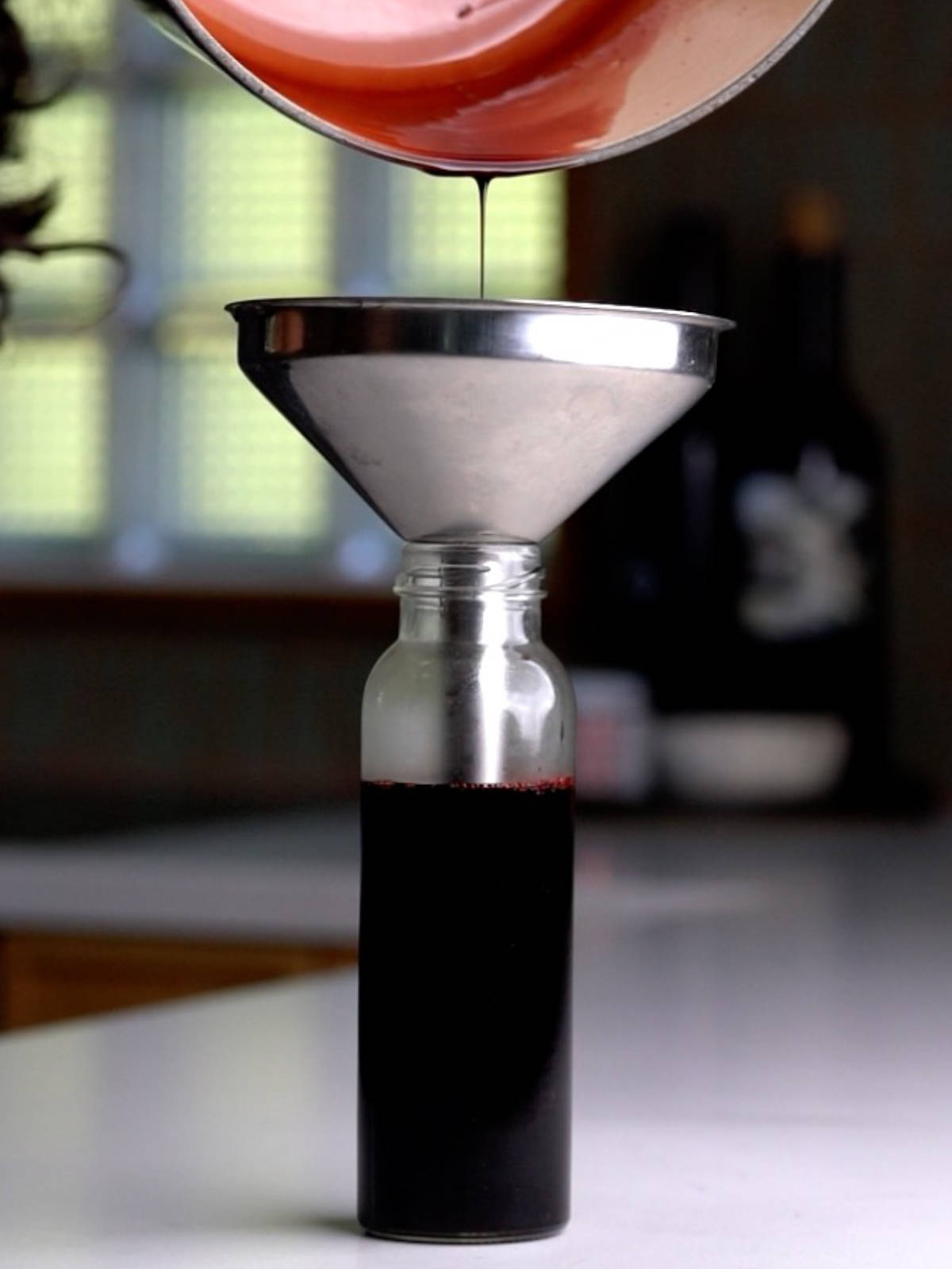 Pouring pomegranate molasses through a funnel into a glass container.