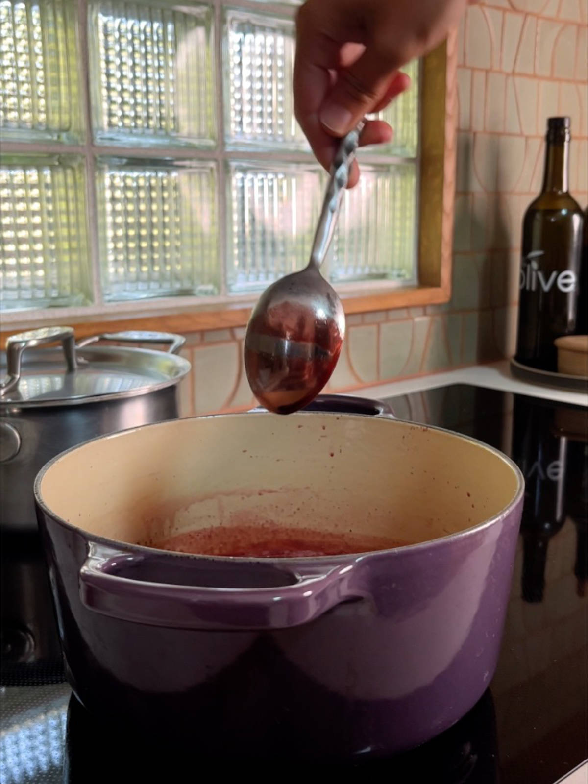 Metal spoon with a space between two layers of pomegranate molasses held over a purple pot.