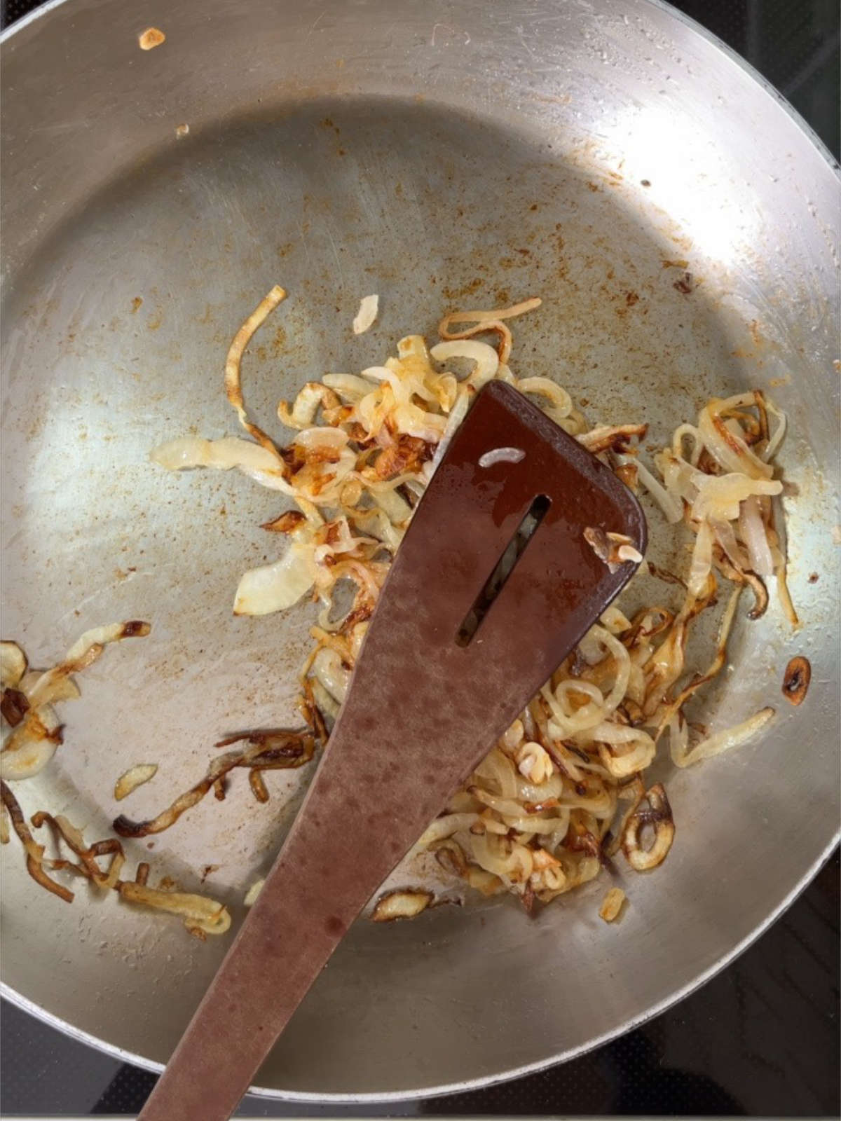 Onions cooking in a metal pan with a wooden spoon.