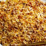 Rice pilaf on a white oval platter with gold serving utensils.