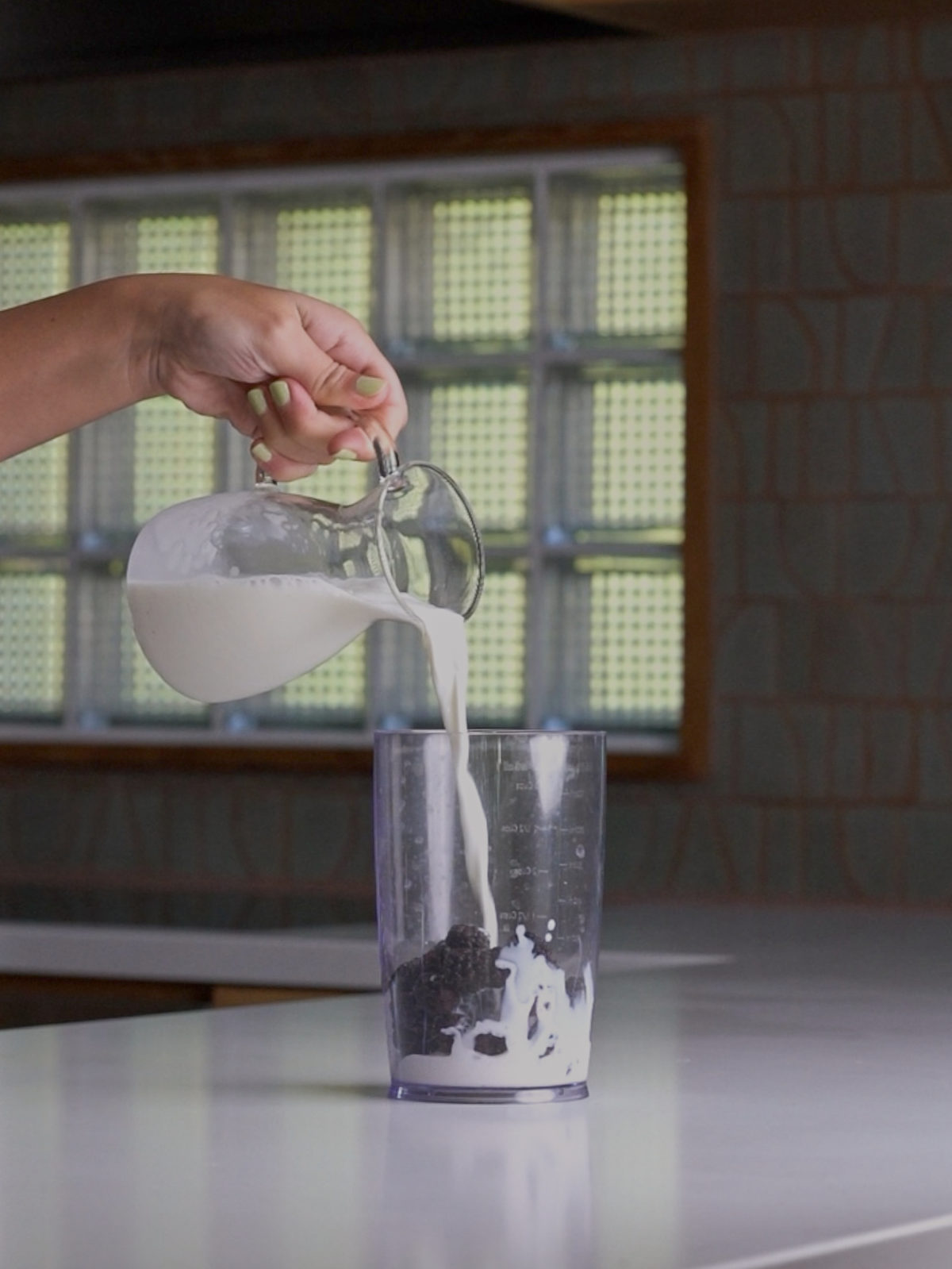 Pouring milk into a clear immersion blender container.