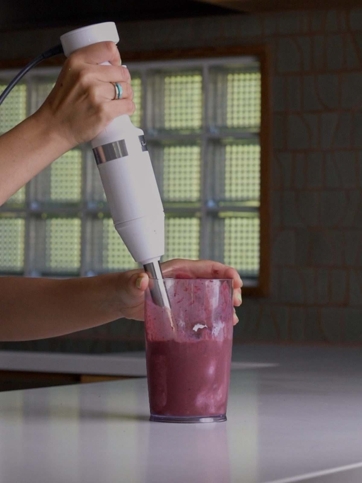 Blending a thick, purple liquid using a white immersion blender.