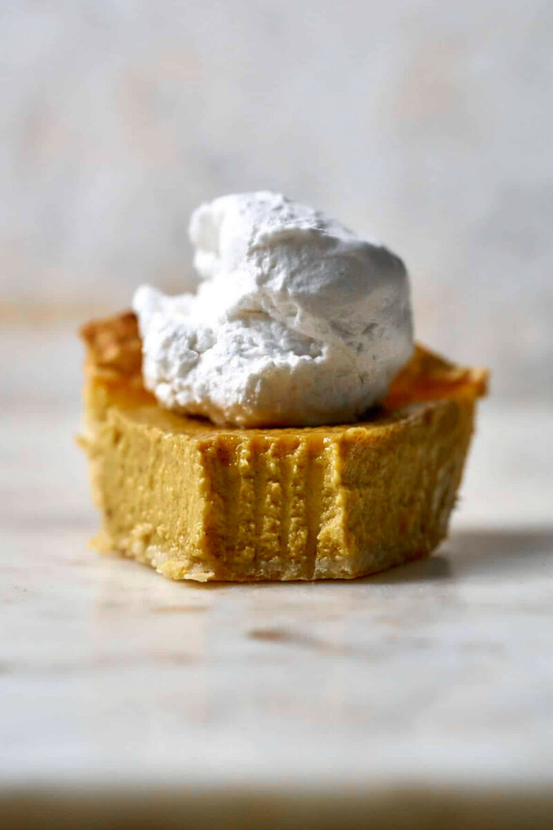 Front view of a slice of pumpkin pie with whipped cream on top.