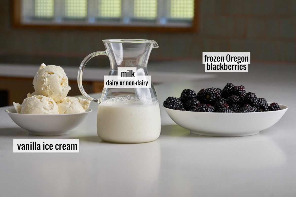 PItcher of milk next to blackberries and three scoops of vanilla ice cream in a bowl.