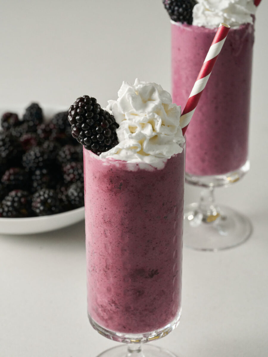 Two purple milkshakes next to a bowl of blackberries.