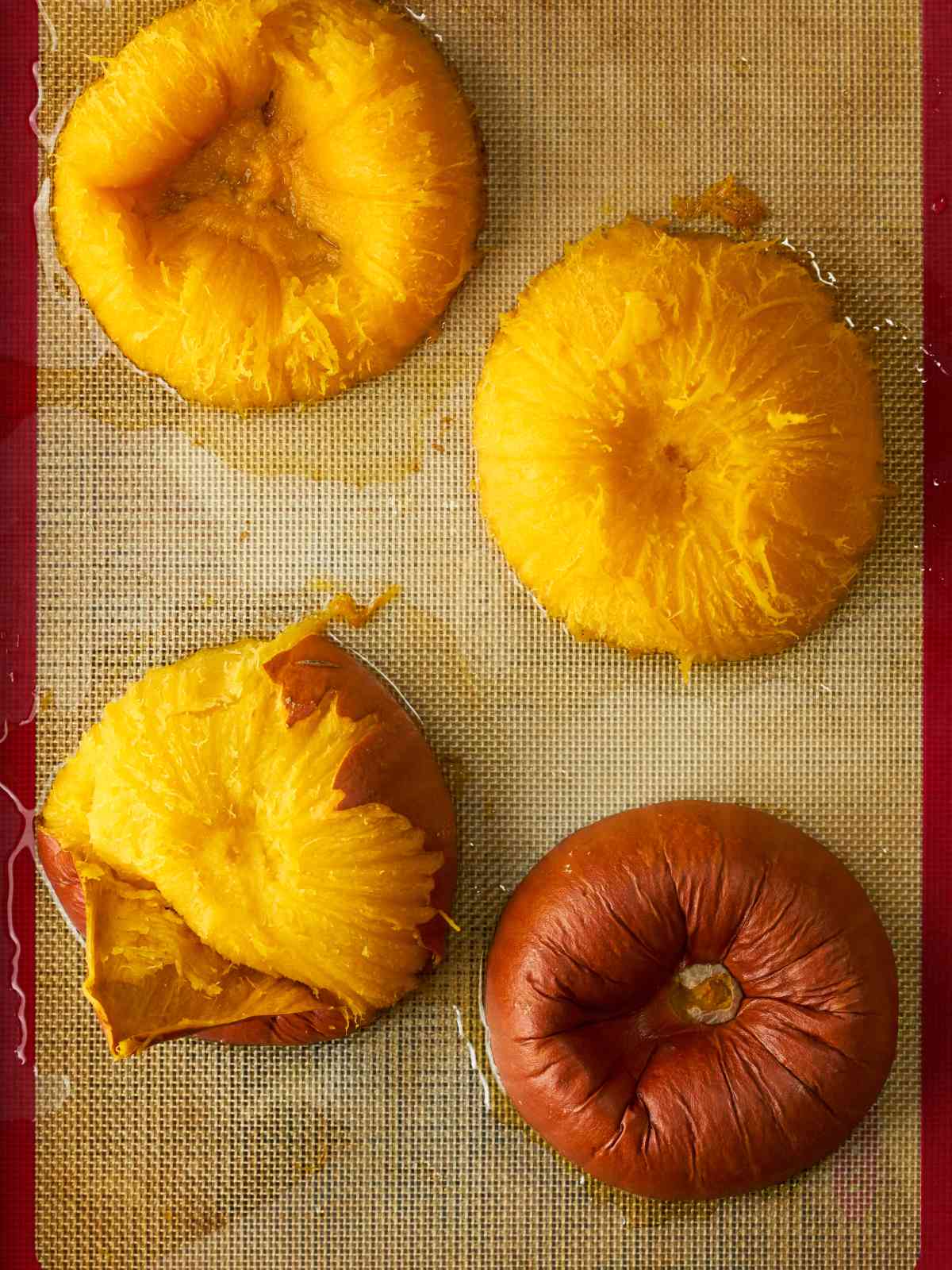 Four peeled and cooked pumpkin halves cut side down on a silicone baking sheet.