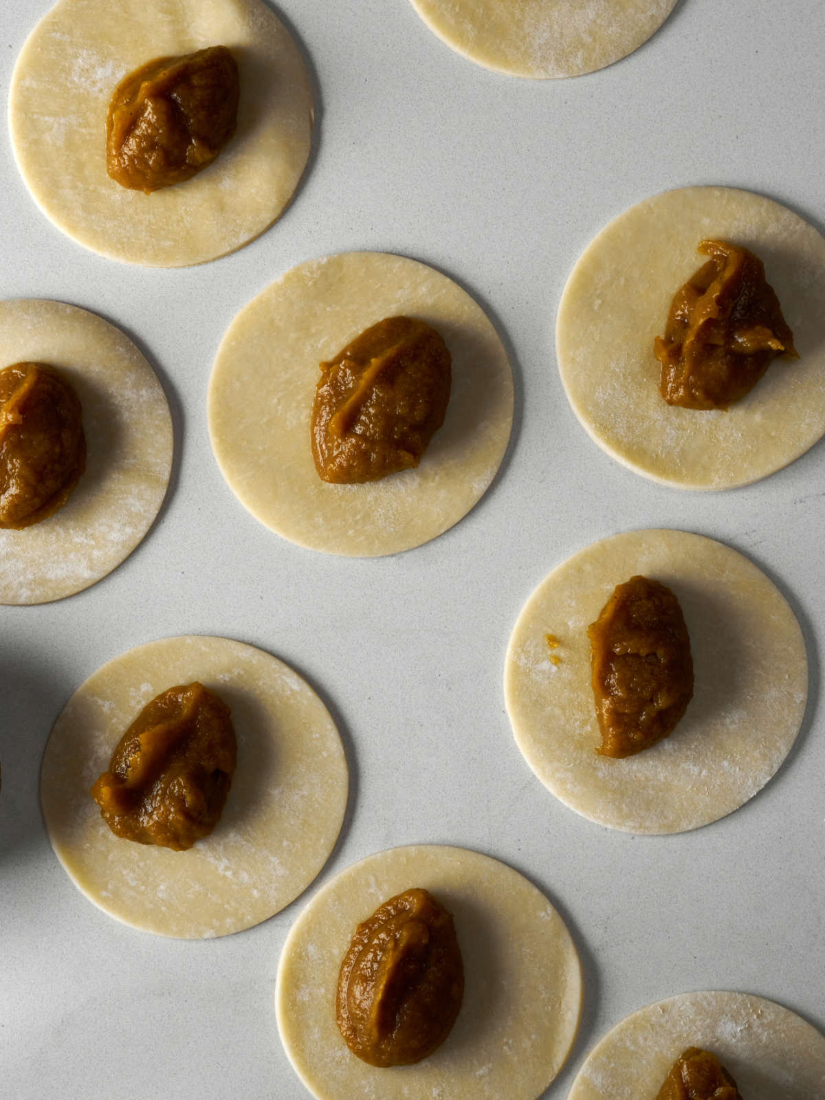 Circles of pie dough topped with dollups of pumpkin pie filling on a countertopl.