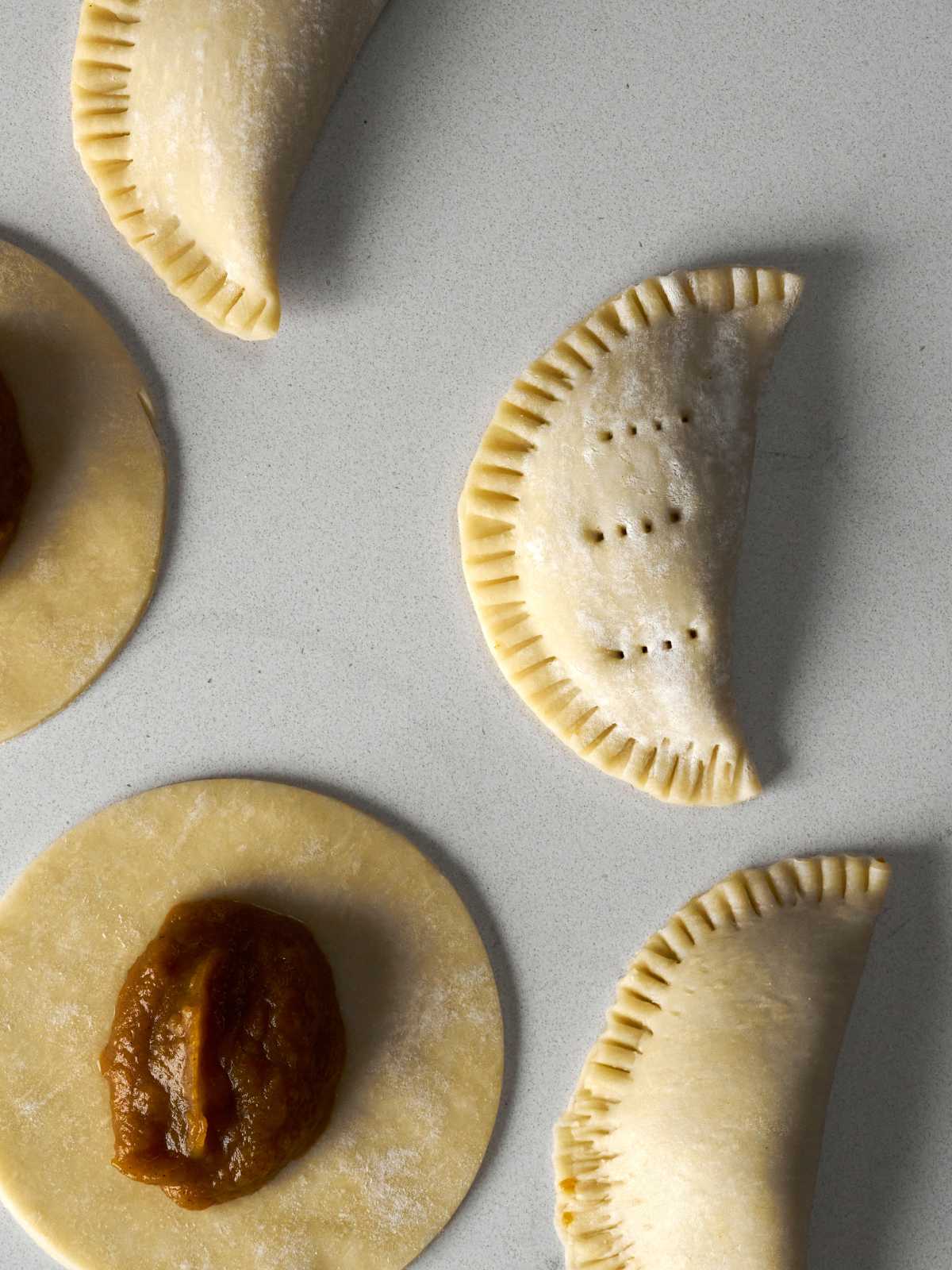 Crimped hand pies next to circular pie dough with dollups of pie filling.