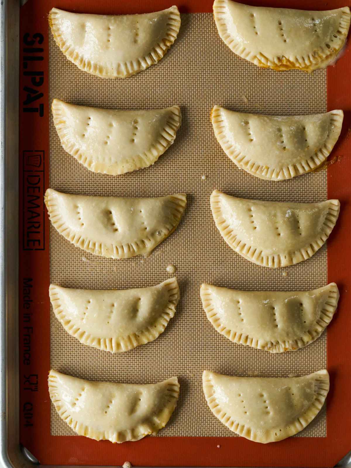 Ten crimped hand pies on a silicone baking mat.