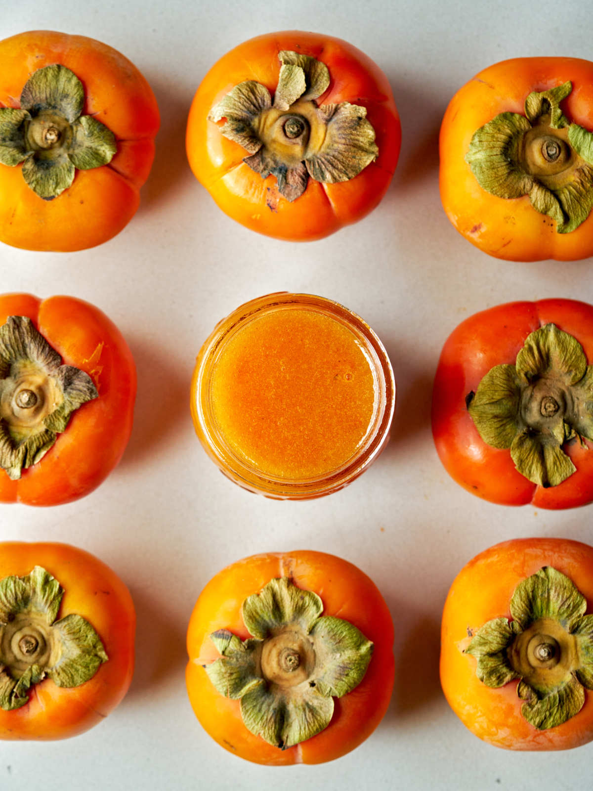 Top view of a jar of orange jam surrounded by a grid of persimmons.