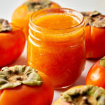 Jar of orange jam surrounded by Fuyu persimmons.