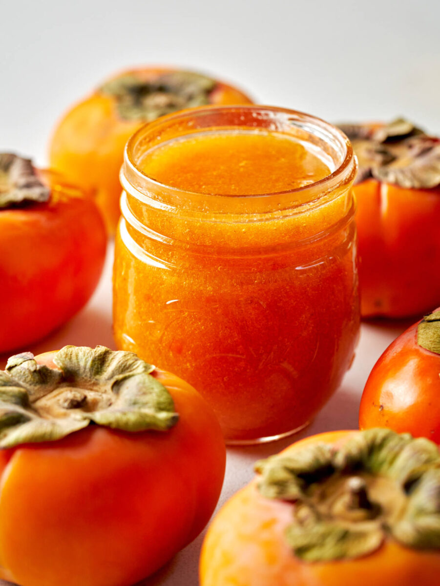 Jar of orange jam surrounded by Fuyu persimmons.