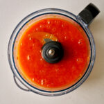 Food processor bowl filled with orange puree.