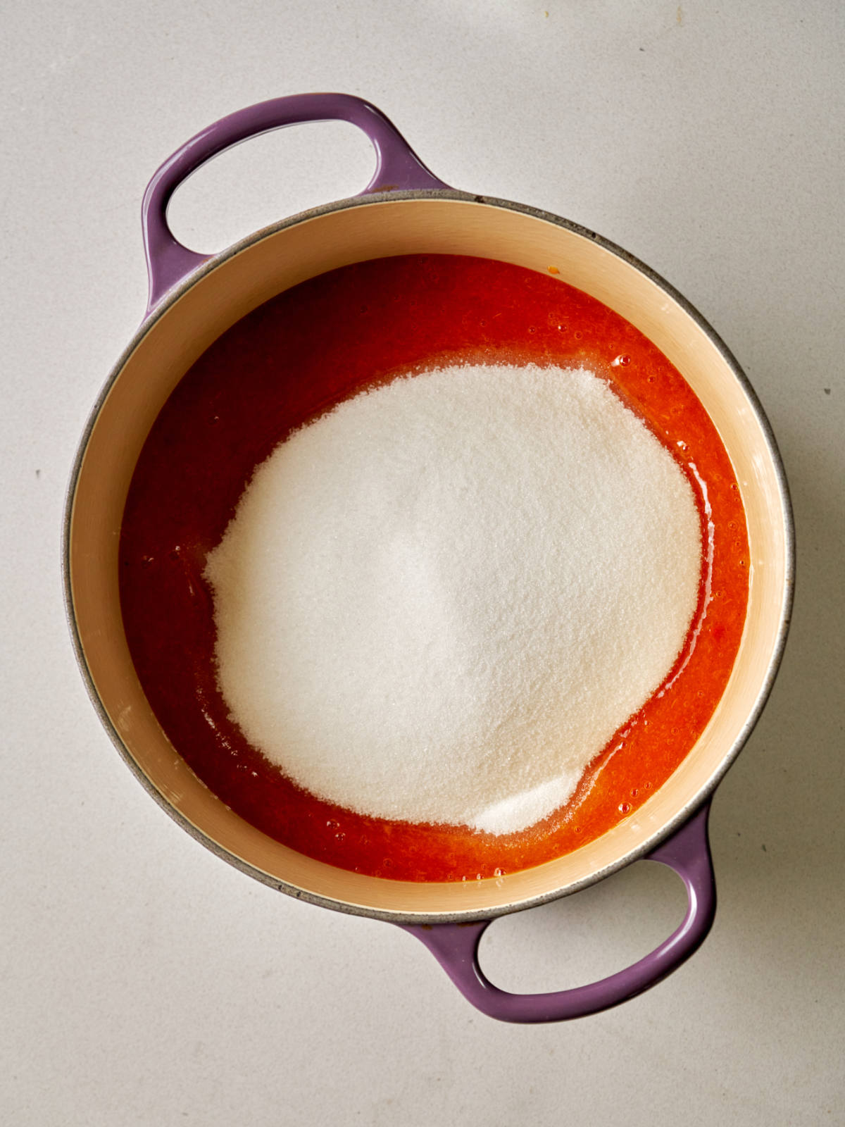 Orange puree in a purple enameled pot with a pile of sugar on it.