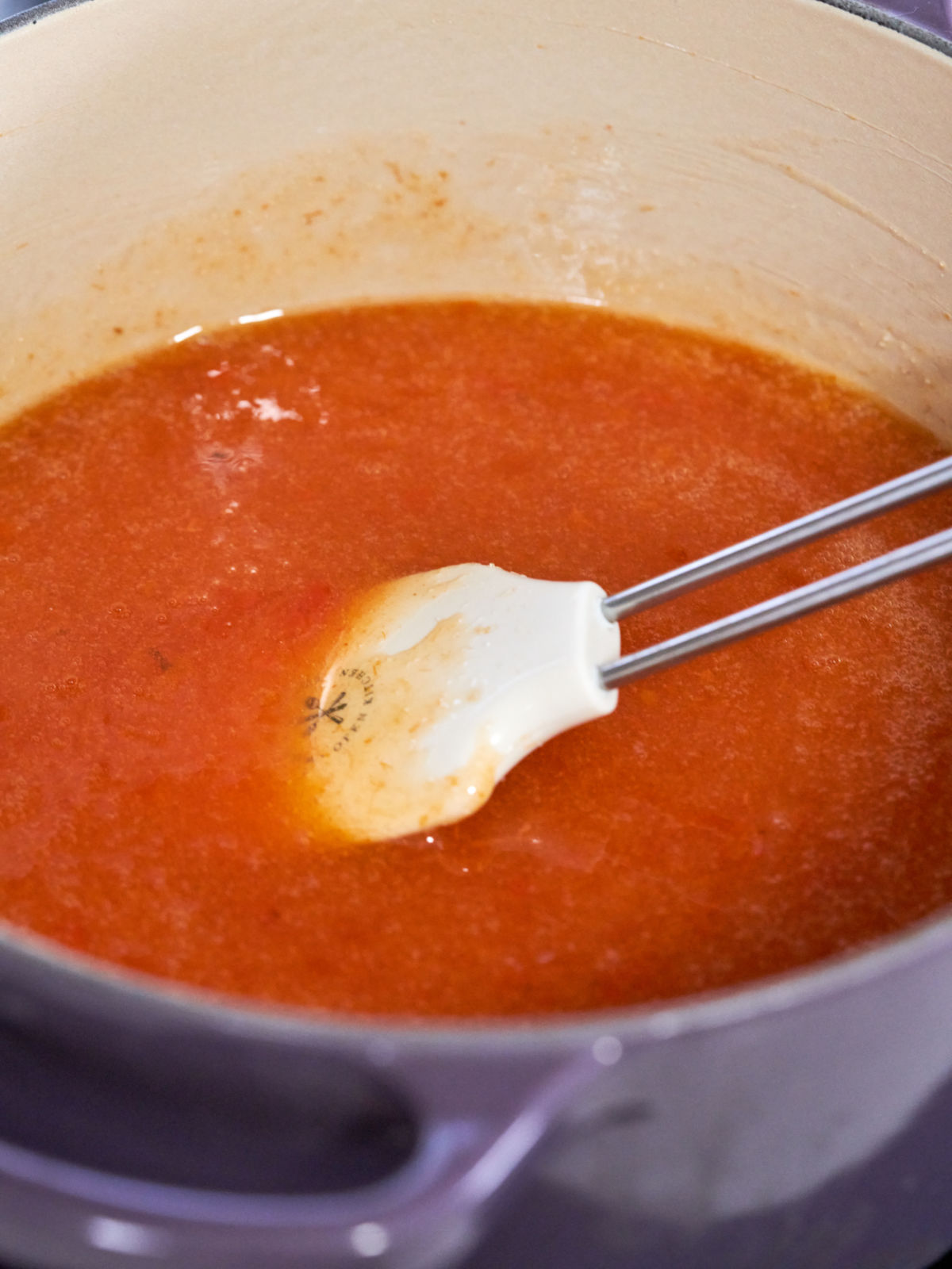 White rubber spatula in a purple pot filled with orange puree.