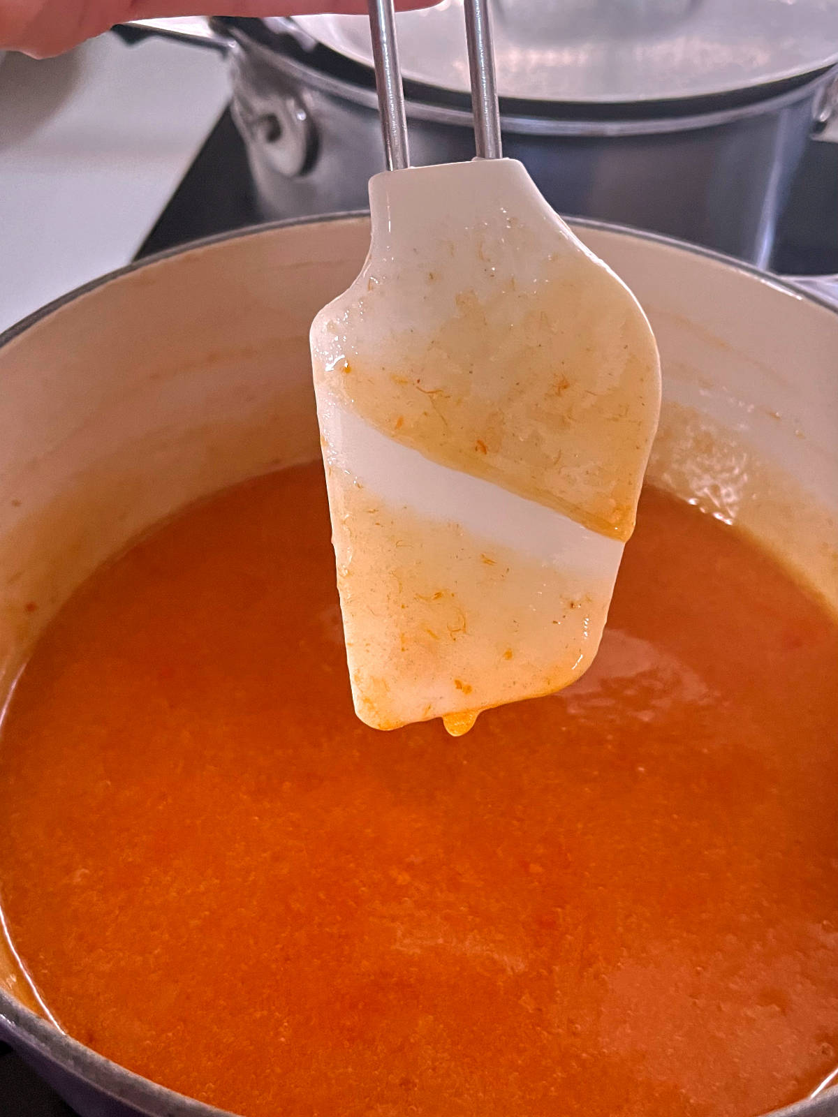 White rubber spatula held over a pot of jam with a line dawn through the middle.