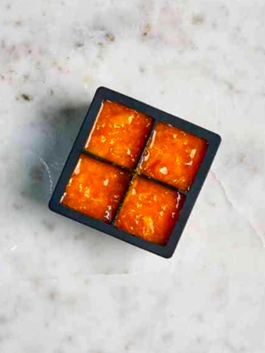 Black ice cube tray with four cubes filled with orange puree.