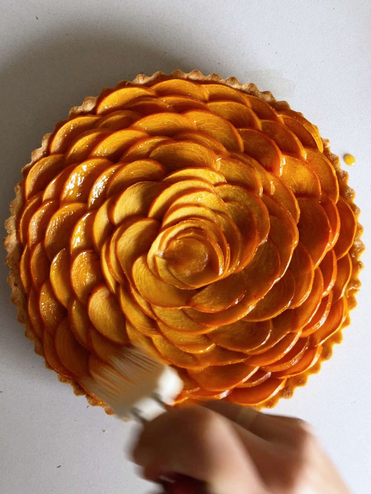 Brusing a tart with orange fruit arranged like a rose with a white pastry brush.
