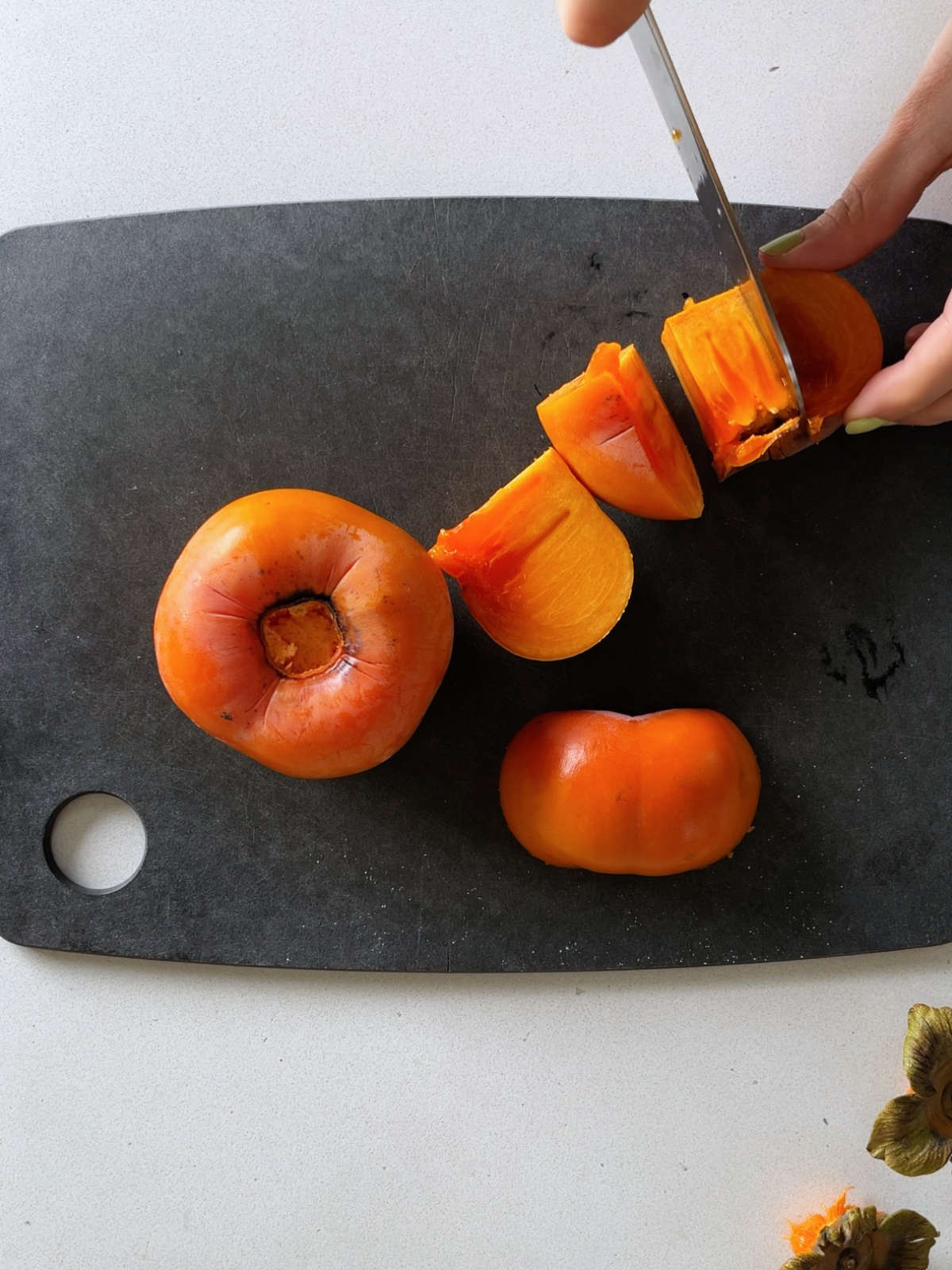 Cutting the center out of a Fuyu persimmon on a black cutting board.